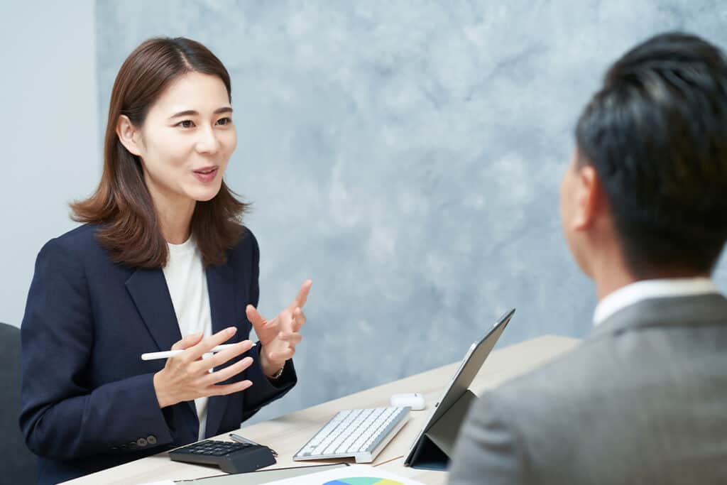 説明するスーツ姿の女性と説明を受ける男性の後ろ姿